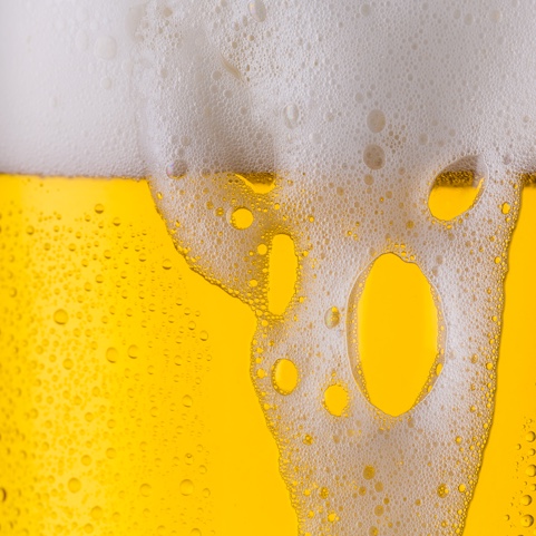 Ein Glas mit gelber Flüssigkeit wird von weißem Schaum bedeckt.