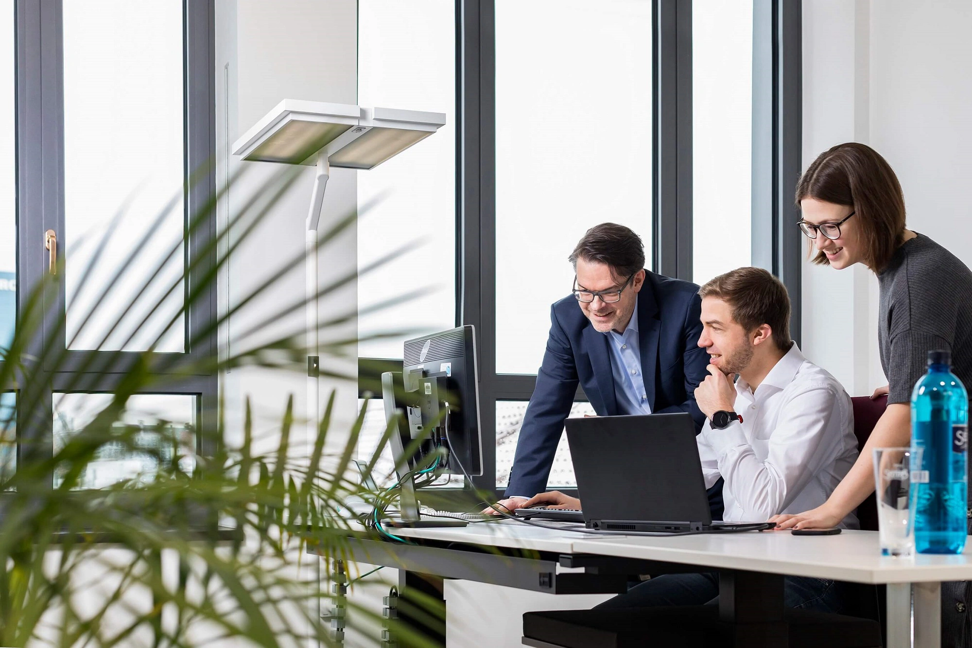 Drei Kollegen betrachten gemeinsam Inhalte auf einem Laptop in einem Büro.
