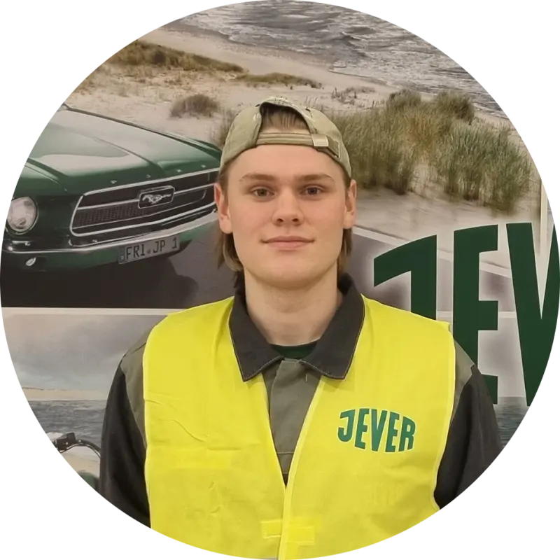 Ein junger Mann mit Kappe steht vor einem Jever-Plakat und trägt eine neongelbe Weste mit Jever Logo.