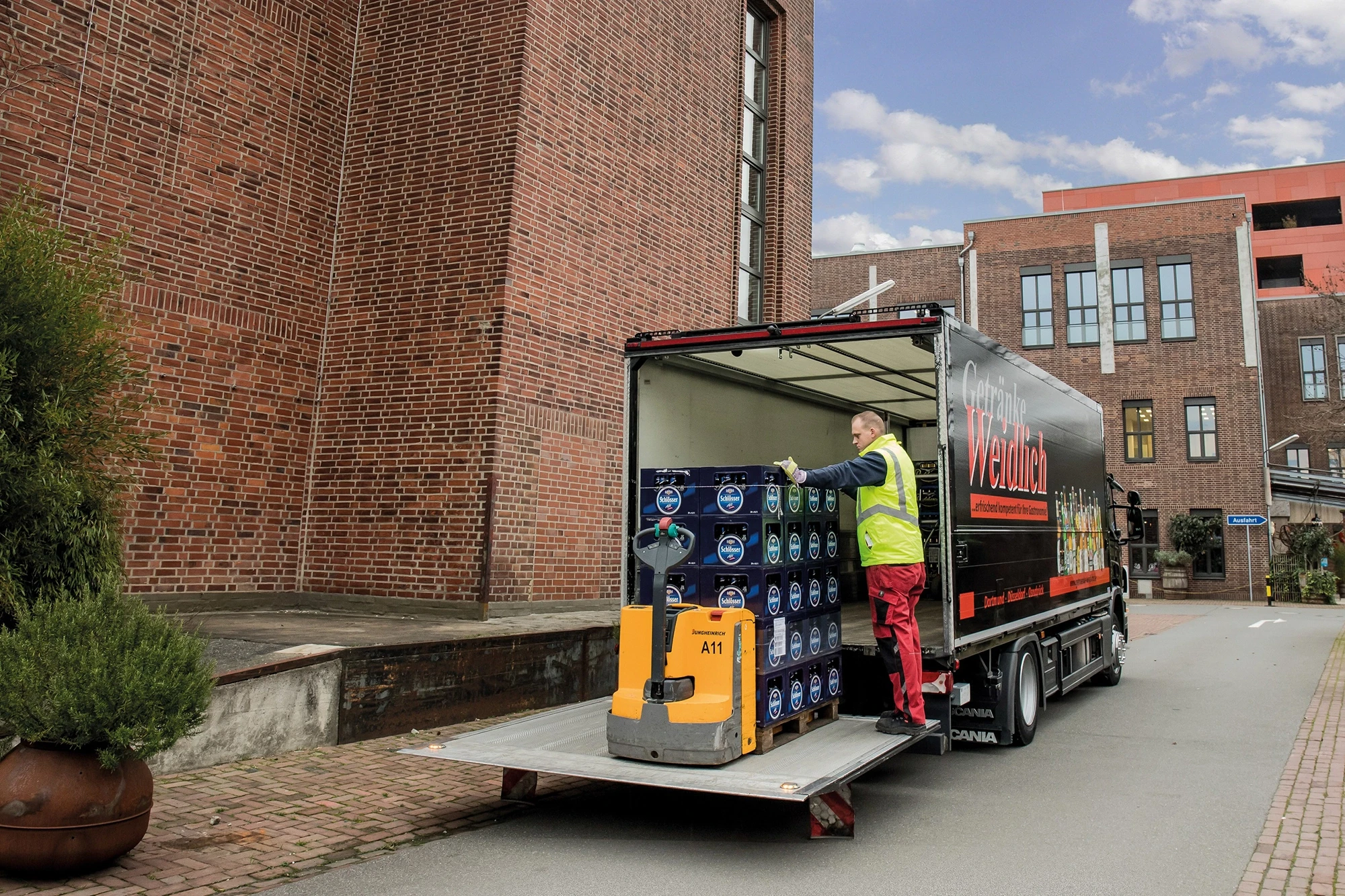 Ein Arbeiter entlädt Getränkekisten von einem LKW in einer städtischen Umgebung.