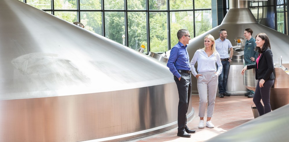 Mehrere Personen unterhalten sich in einer Brauerei mit großen Edelstahltanks.
